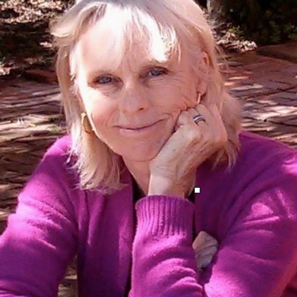 Smiling woman in a purple sweater with hand on chin outdoors.