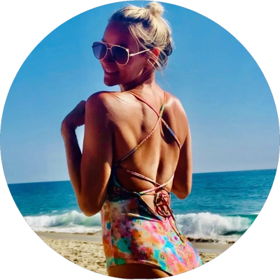 Woman in colorful swimsuit smiling on a sunny beach with ocean waves.