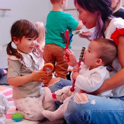 A mother smiles at her two young daughters, who are happily playing with instruments