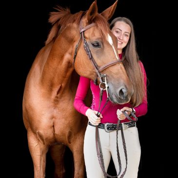 Woman standing with a brown horse against a black background.