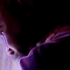 Close-up of a person's face in low light with purple hues.