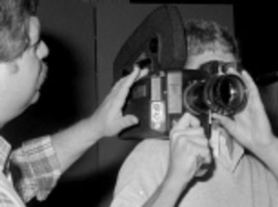A black-and-white close-up showing a person operating a vintage handheld film camera.