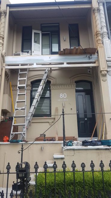 Renovation work on a beige townhouse with ladders and tools outside.