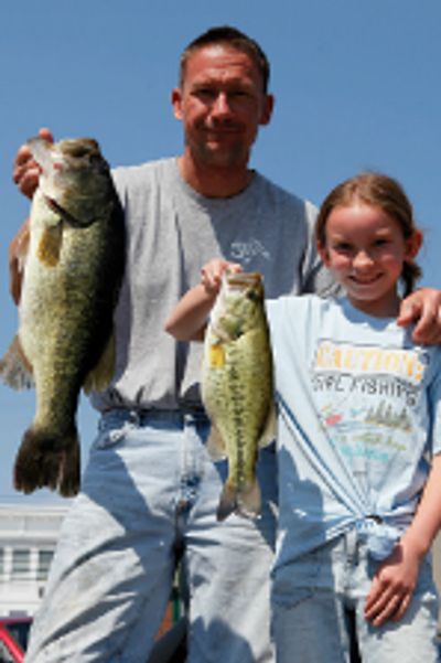 A man and a girl proudly hold up their caught fish outdoors.