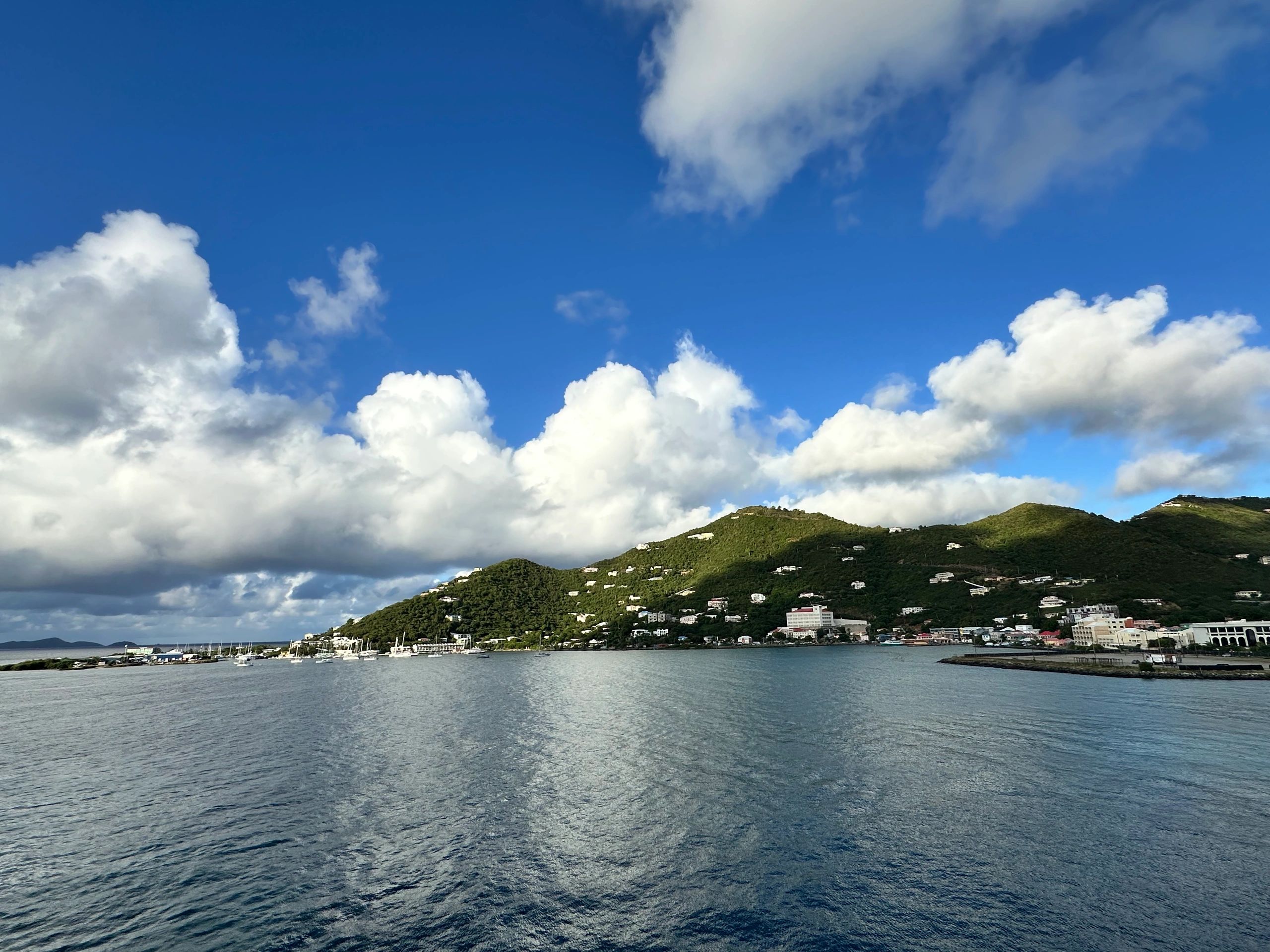 Coastal town with green hills under a blue sky with fluffy clouds.