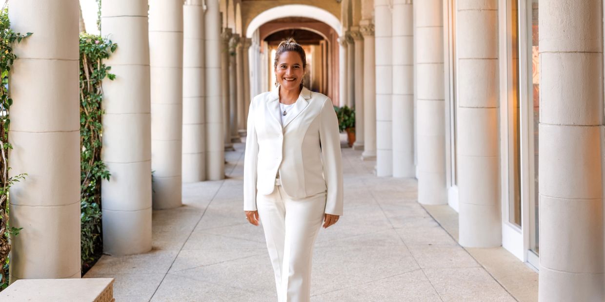 Woman in white suit standing in archway corridor.