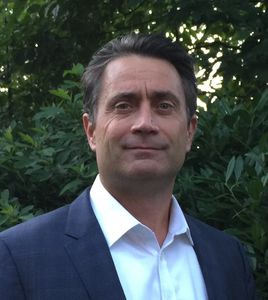 Man in blue suit and white shirt in front of trees