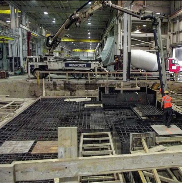 Concrete pump truck pouring a concrete foundation in a facility.