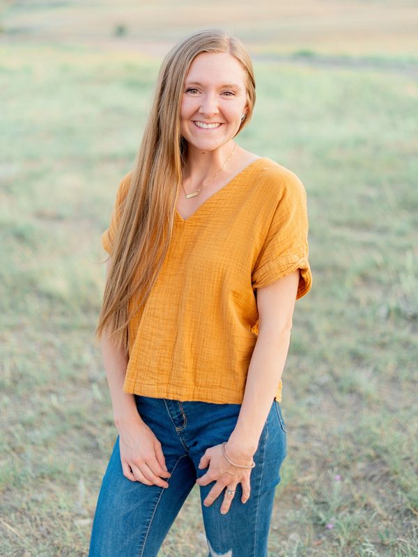 Smiling woman in yellow top and jeans outdoors.