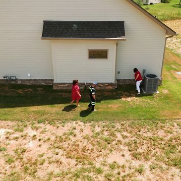 Three people inspecting the side of a house with patchy grass.