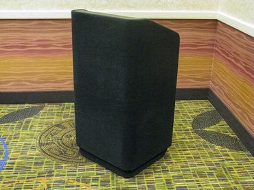 Black covered podium in a corner with patterned carpet and wall.