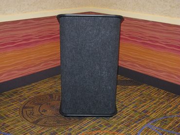 A black speaker positioned in a corner with colorful carpet and wall patterns.