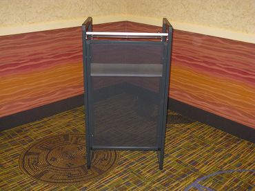Black mesh podium or lectern in a corner with patterned carpet and colorful wall decor.