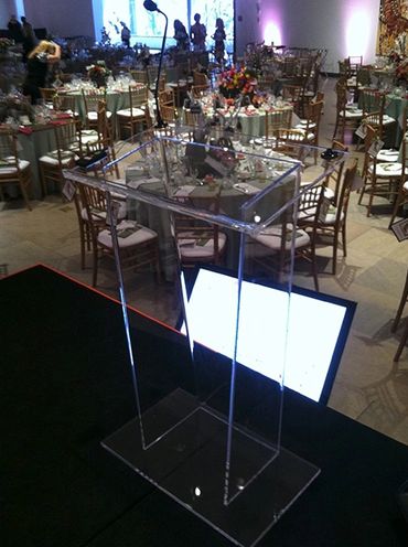 Clear acrylic podium on a stage in a decorated event hall.