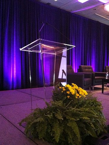 Transparent podium with floral arrangement on stage under purple lighting.