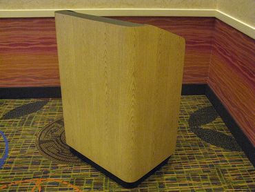 Wooden podium in a corner on patterned carpet.