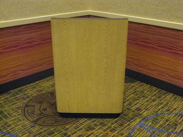 A wooden podium placed in a carpeted corner of a room.