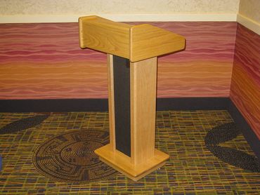 Wooden podium with a black panel in a colorful room corner.