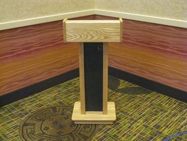 Wooden podium with black panel in a carpeted conference room corner.