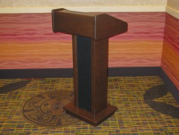 A wooden podium stands on a patterned carpet against a colorful wall.