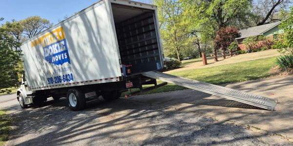 A moving truck with a ramp extended parked near a house on a sunny day.