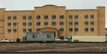 Large brown building with multiple windows and vehicles outside.