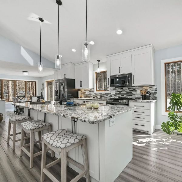 Bright modern kitchen with island, white cabinets, and large windows overlooking trees.