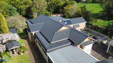 Aerial view of a house with dark gray metal roofing surrounded by greenery.