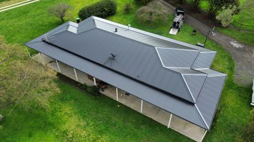 Aerial view of a house with a metal roof surrounded by green grass.