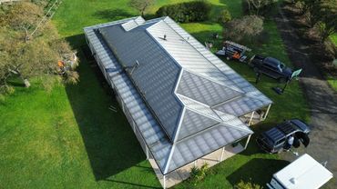 Aerial view of a house with a corrugated metal roof and vehicles nearby.