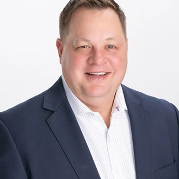 Smiling man in a navy blazer and white shirt.