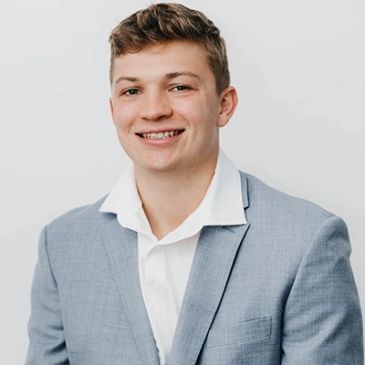Young man in a light gray suit smiling.