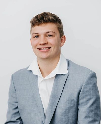 Young man in a light gray suit smiling.