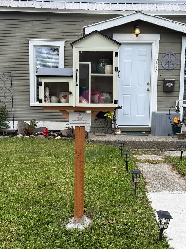 A small outdoor cabinet for sharing pottery items in front of a house.