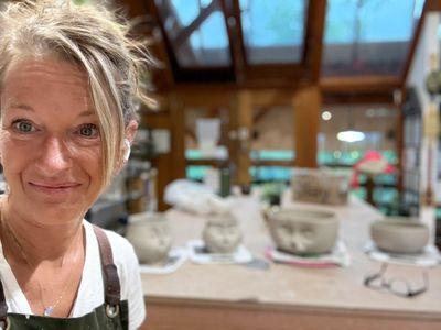 Woman smiling in a pottery workshop with clay sculptures in the background.