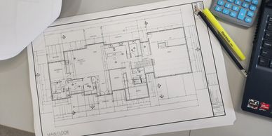 residential drafting blueprints on a table with hard hat, pencils, and calculator