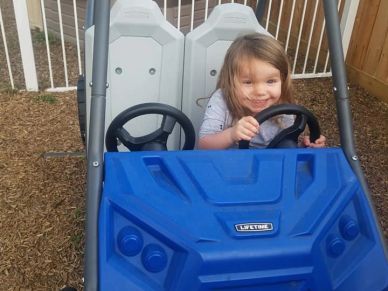 A child smiling and sitting in a blue toy car.