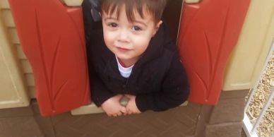 Smiling child peeking through a playhouse window.