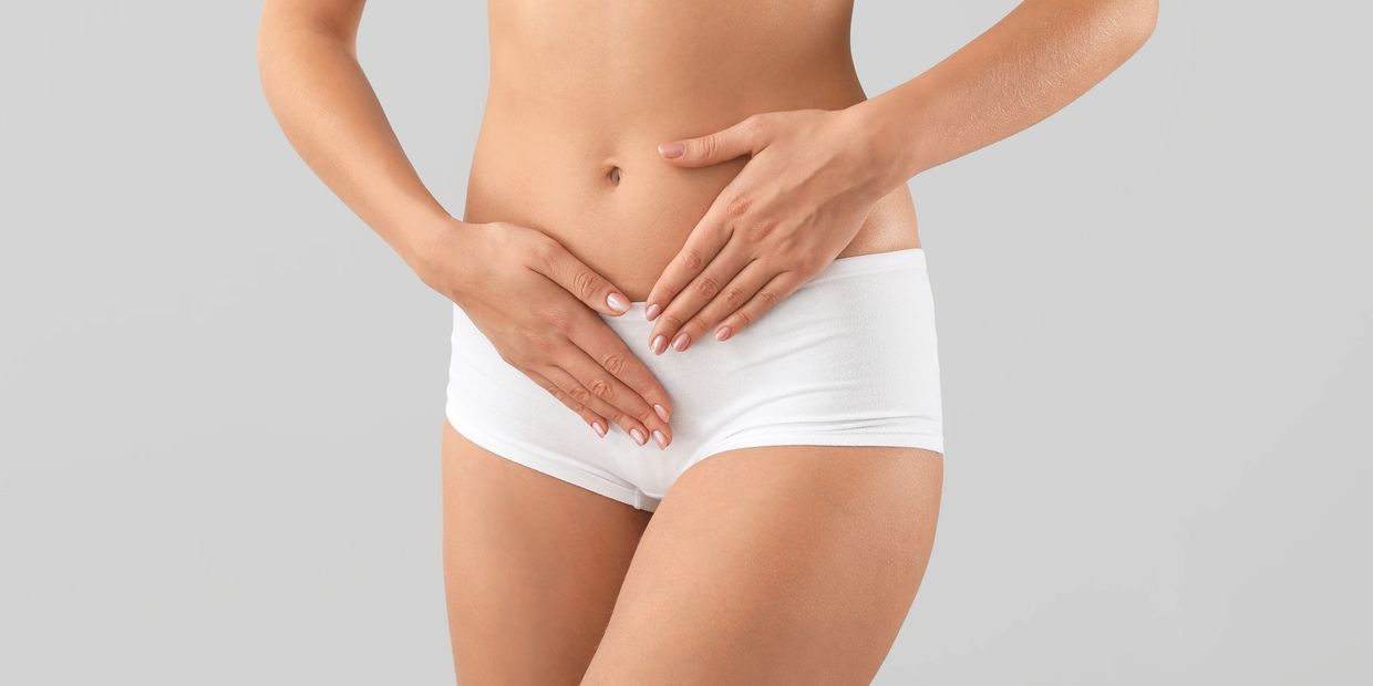 Woman in white shorts holding her lower abdomen, indicating discomfort.