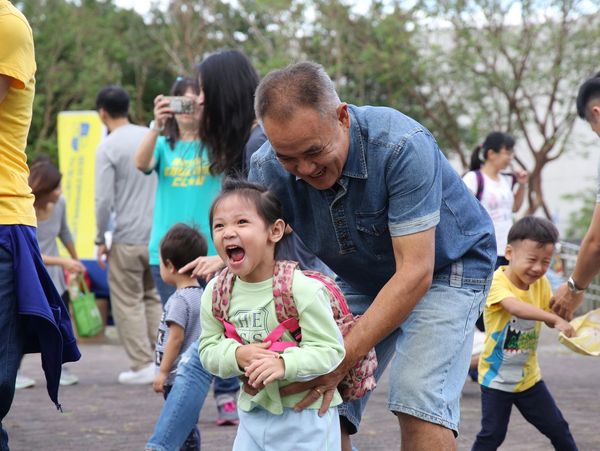 A joyful grandfather playing and laughing with his granddaughter outdoors.