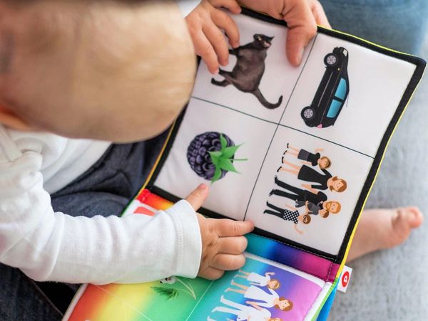 A baby exploring a colorful picture book with family and objects.