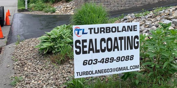 A sign for Turbolane Sealcoating with contact details on a rocky roadside.