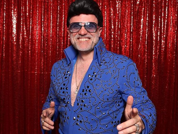 Man dressed as Elvis Presley in blue jumpsuit and sunglasses.