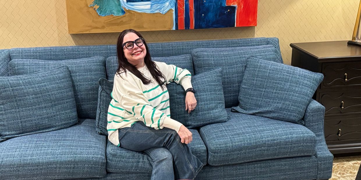 Smiling woman sitting on a blue sofa with large glasses and casual attire.
