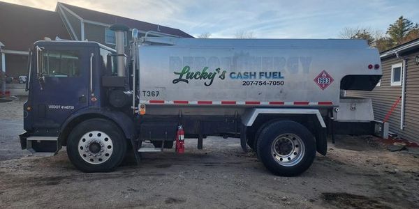 A large fuel delivery truck parked on a dirt surface near buildings.
