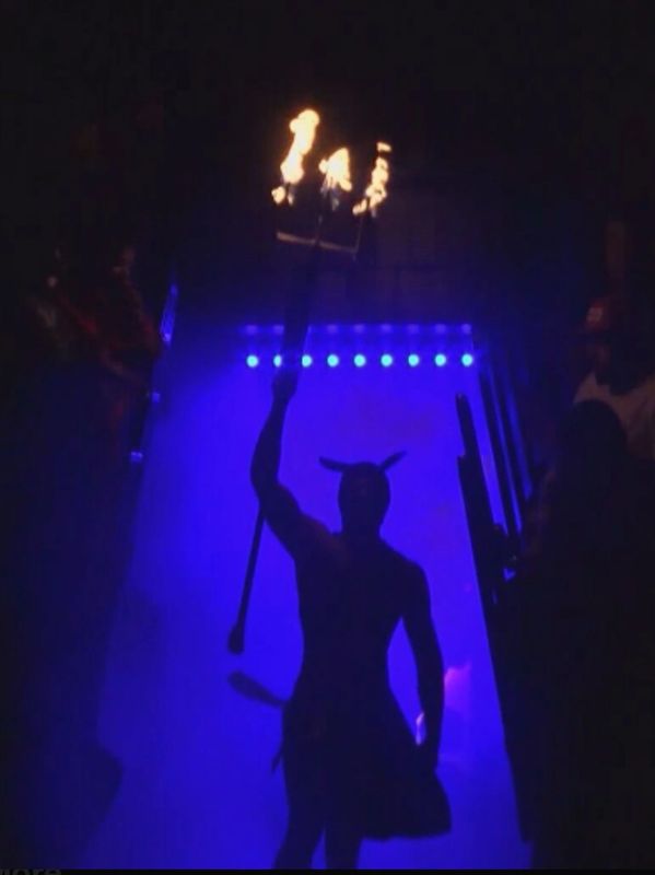 Silhouetted figure with horns holding a flaming trident against blue light.