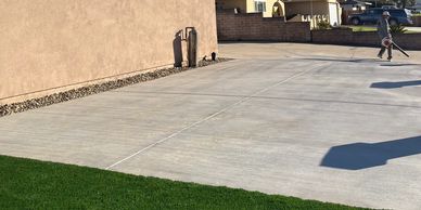 A person walking on a large concrete driveway beside a house and green lawn.
