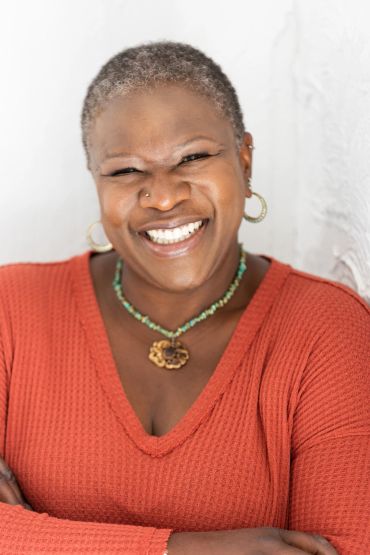 Smiling woman in orange sweater with short hair.