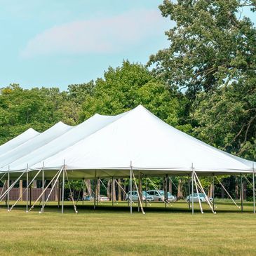 Large white tents set up on a grassy field near trees and parked cars.