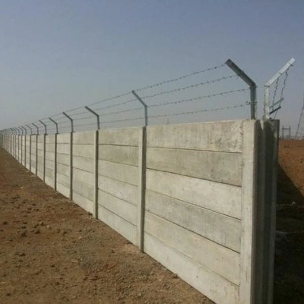 Long concrete wall topped with barbed wire in a barren area.